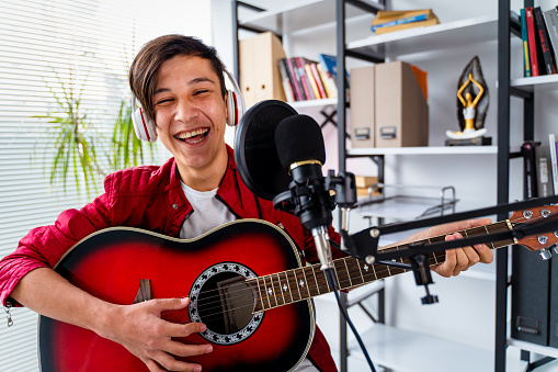 teenager boy vocalist Wearing Headphones with a Guitar recording a song front of microphone