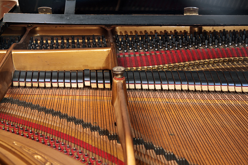 Inside a grand piano with metal frame, strings, hammer and damper, view into the mechanics of an older acoustic musical instrument, concept for music and culture, selected focus, narrow depth of field