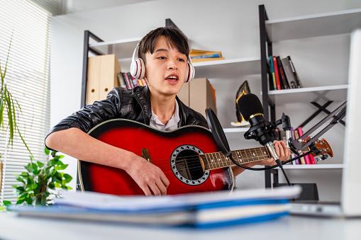 teenager boy vocalist Wearing Headphones with a Guitar recording a song front of microphone
