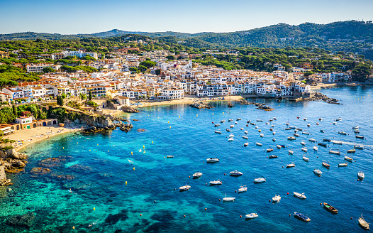 aerial view of Calella de Palafrugell old village in a summer morning with a blue sea and sky with a lot of little boats parked in front. Costa Brava, Girona province, Catalonia. Spain