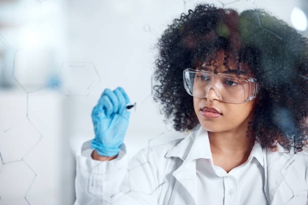 istock One serious young mixed race female scientist with a curly afro writing and planning on a glass board wearing glasses and gloves at work. Focused hispanic lab worker drawing on a board 1432920896