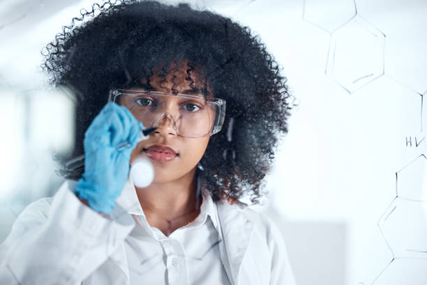 istock Focused young scientist brainstorming, thinking of ideas in the lab. Young chemist working on her research formula, writing on a board. Female biologist drawing a dna chain on a board to find cure 1432920908