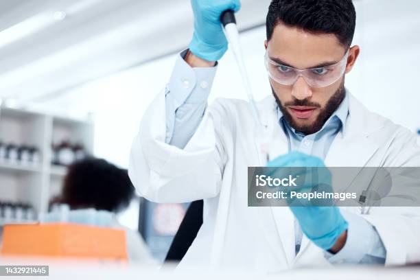 One Mixed Race Male Scientist Wearing Safety Goggles And A Labcoat While Conducting A Medical Research Experiment With Pipette And Test Tubes In A Lab Recording His Findings For Future Investigation Stock Photo - Download Image Now