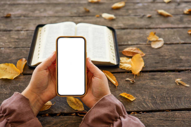 istock Open bible and phone with isolated screen on wooden background 1432921553