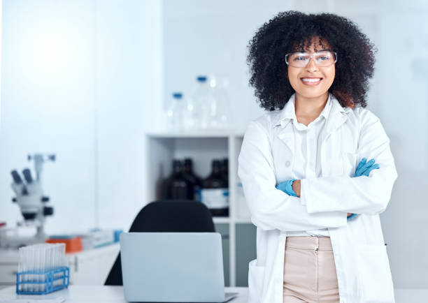 porträt einer stolzen afroamerikanischen wissenschaftlerin mit schutzbrille in ihrem büro. lächelnde ärztin mit verschränkten armen in einem laborkittel im labor. leistungsstarker wissenschaftlicher experte bei der arbeit - lab coat women one person female stock-fotos und bilder