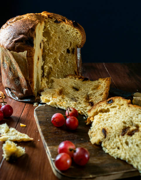istock High angle of a cut panettone on a wooden table with grapes decorating, selective focus, black background, vertical, with copy space. Christmas atmosphere 1432925385