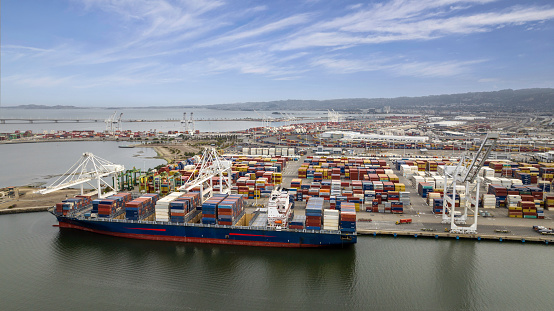 Aerial stock photos of large scale commercial shipping cargo container ships moored in Oakland alongside Alameda California.