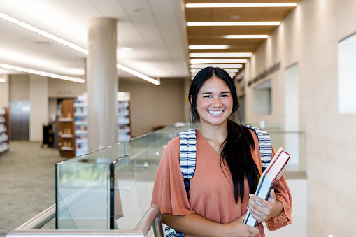 The smiling teenage girl, carrying her textbook, stops to smile for the camera.