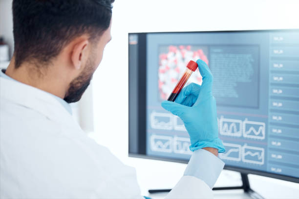 未知の混血の医学者は、研究室に一人で座って、血液のバイアルを持ち、コンピュータを使ってそれを調べました。診療所で試験管サンプルを分析するヒスパニック系の医療従事者 - vial laboratory test tube biotechnology ストックフォトと画像