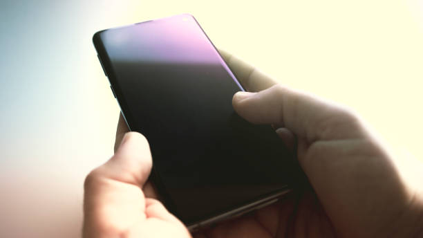 istock Black mobile phone turned off on a white table with a man's hands next to it waiting for a call 1432929450