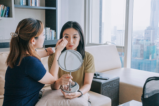 Asian Chinese female makeup artist with disability deformed arm drawing eyebrows for her friend at home