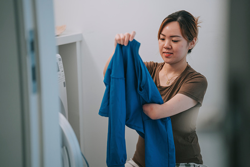 Photo of a young woman putting laundry in a washing machine from above