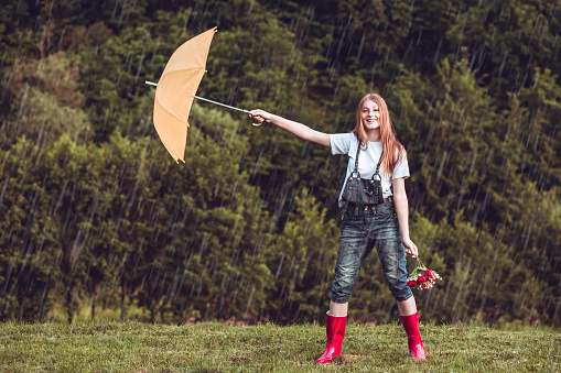 Smiling young woman under blue umbrella outdoors in the rain