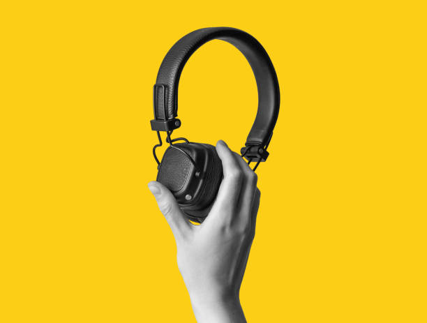 istock Black wireless headphones in hand on bright yellow background 1432941059