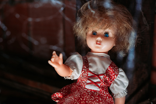 Old doll with scary look in red dress with blue eyes and with spider web in front of her. Halloween concept