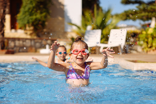 Child learning to swim in outdoor pool of tropical resort. Kids learn swimming. Exercise and training for young children. Little boy with colorful float board in sport club. Swimming baby or toddler.