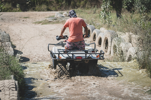 Rear view of young men riding  Quad on muddy water