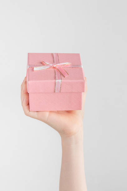 istock Child hand holding gift box with pink bow. white and gray background with copy space 1432943946