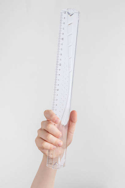 istock child hand holding transparent glass or plastic ruler. white and gray background with copy space 1432943961