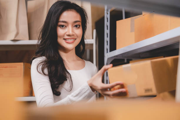 online shopping concept, happy young Asian business owner woman prepare parcel box and check orders of product for deliver to customer on laptop computer at home, e-business marketing on cyberspace concepto de compra en línea, joven y feliz mujer asiática propietaria de negocios preparar la caja de paquetes y verificar los pedidos de productos para entregarlos al cliente en una computadora portátil en casa, marketing de negocios electrónicos en e