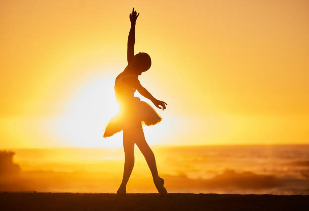 silhouette einer jungen balletttänzerin am strand bei sonnenuntergang. anmutige, schlanke ballerina, die mit leidenschaft tanzt und ihre hand ausstreckt - ballet dancer beautiful dancing beauty stock-fotos und bilder