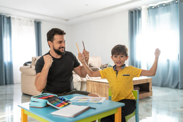 father helps son to do homework at home and they celebrate success with raised hands stock photo