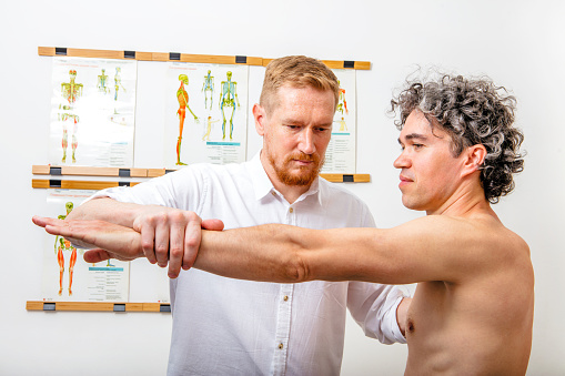 Male osteopath (chiropractor) healing a man by stretching his arm. Can illustrate the concept of Osteopathy, Alternative medicine, Physiotherapy, pain relief.