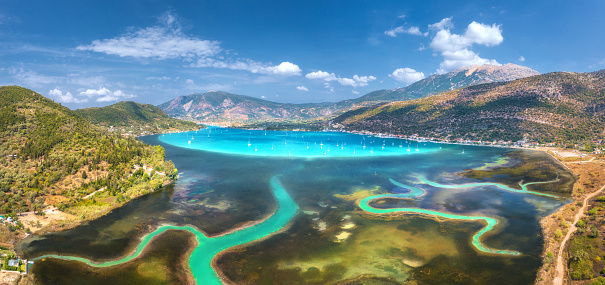 Aerial view of river delta, boats and yachts in blue lagoon, mountains and sky. Summer in Lefkada island, Greece. View from above of river estuary, sea bay, sailboats, rocks, green forest. Colorful