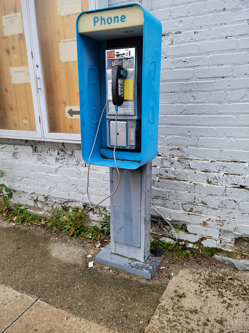 Outdoor pay phone with a cord by an old brick building