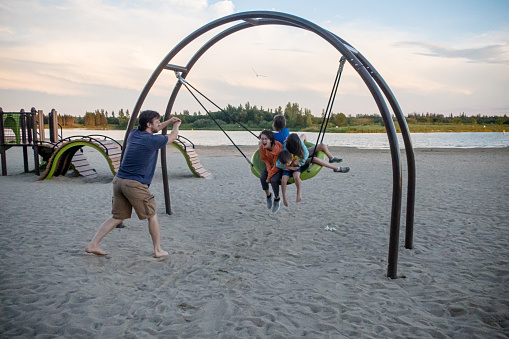 going to the beach with kids at birds hill park, Manitoba Canada. A parent is swinging 4 kids on this birds nest style swing at the beach.
