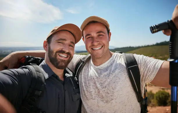 Photo of Friends, brothers or hikers taking a selfie while hiking outdoors in nature sharing the experience on social media. Active, fit and athletic men take a picture or a photo while trekking