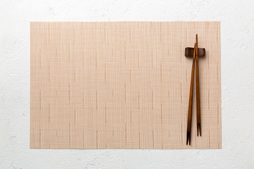 Two chopsticks and bamboo mat on cement background. Top view, copy space.