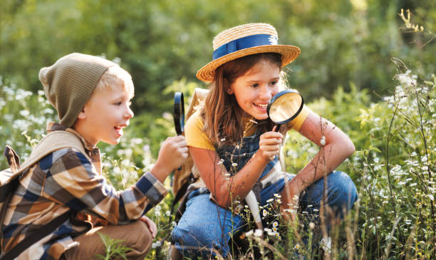 istock Two little kids with backpacks examining plants through magnifying glass in forest 1432973621