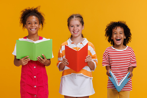 Group of cheerful happy multinational children schoolkids with books on colored yellow background