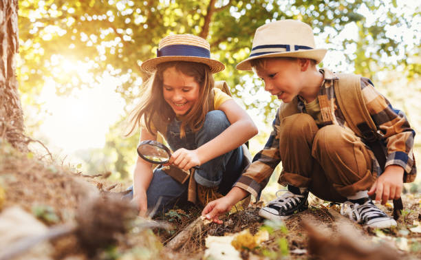 istock Two little kids with backpacks examining plants through magnifying glass in forest 1432974577