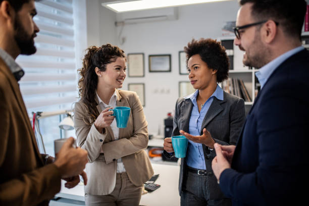 istock Group of smiling colleagues standing at workplace, chatting and drinking coffee on pause 1432974591