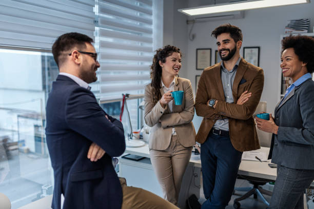 istock Group of smiling colleagues standing at workplace, chatting and drinking coffee on pause 1432976080