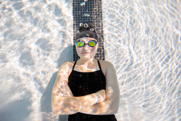 Underwater view of young female swimmer laying down at the bottom of the pool with arms cross looking at camera
