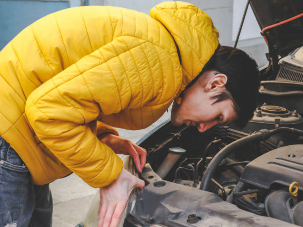 młody kaukaski facet w żółtej kurtce sprawdza wewnętrzną awarię z otwartą maską samochodu - hood car headlight bumper zdjęcia i obrazy z banku zdjęć