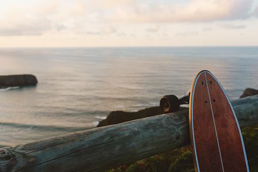 skateboard, surf skate or longboard skate, leaning on a wooden railing with the sea and the beach in front at sunset. Outdoor and summer sports concept.