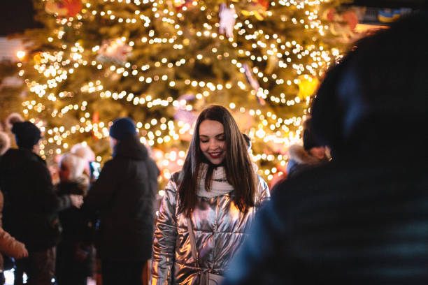 Happy young woman standing by Christmas tree in city at night stock photo