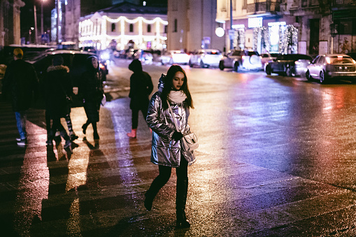 Young woman crossing road in city during winter at night