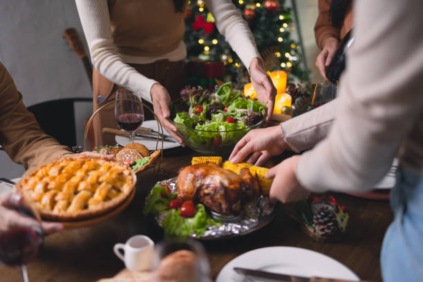 Asian Young men and women enjoy roasted turkey and vegetable meal Family at Thanksgiving dinner. Asian Young men and women enjoy roasted turkey and vegetable meal. Asia people group serve food and decoration christmas table setting at home at night. big family table stock pictures, royalty-free photos & images