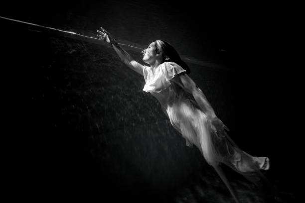 Black and white underwater image of a young woman going towards the light while wearing a white dress.