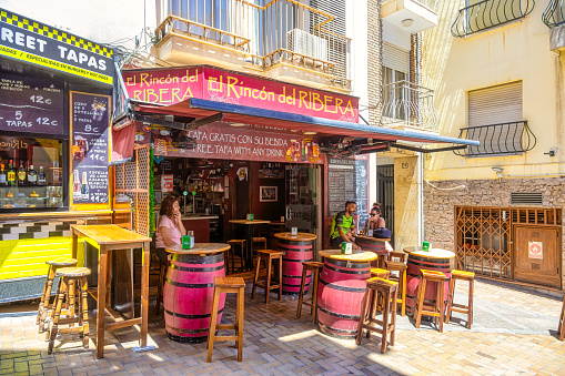 Benidorm, Spain - August 21, 2022: People relaxing and drinking at an outdoor bar on a sunny day. The bar has a sign that says \