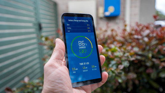 A man checks the charging status of a home installed battery storage unit on a smartphone