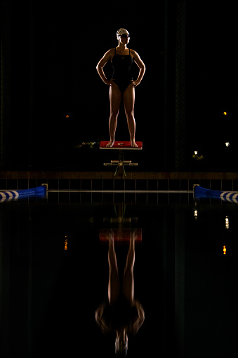 Female swimmer ready to swim standing on a  starting block at night time