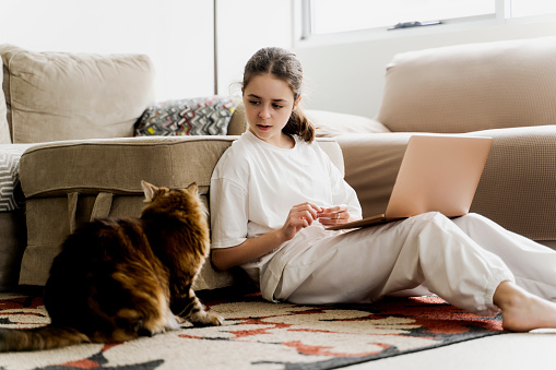 The young girl is studying at home and the cat wants to play with her