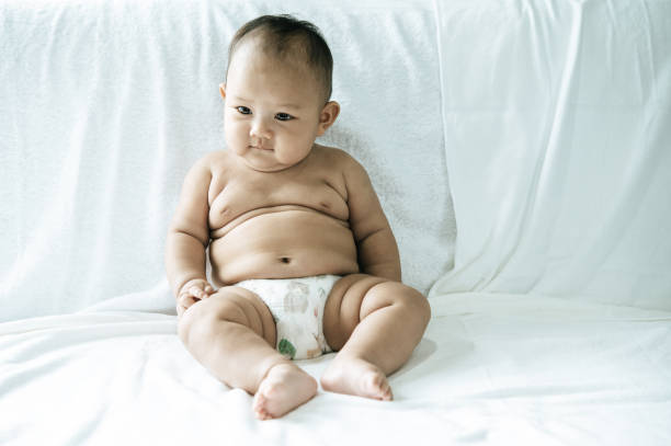 Baby chewing on clothes while lying on a sofa, with parent holding clothes in background