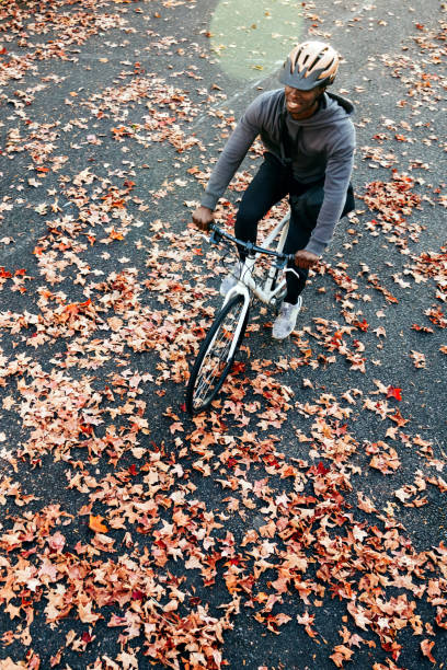 An adult African American man enjoys a bicycle ride on a brisk and sunny autumn day in the Pacific Northwest.   The fall leaves glow in the sunlight. Shot in Seattle, Washington, USA.